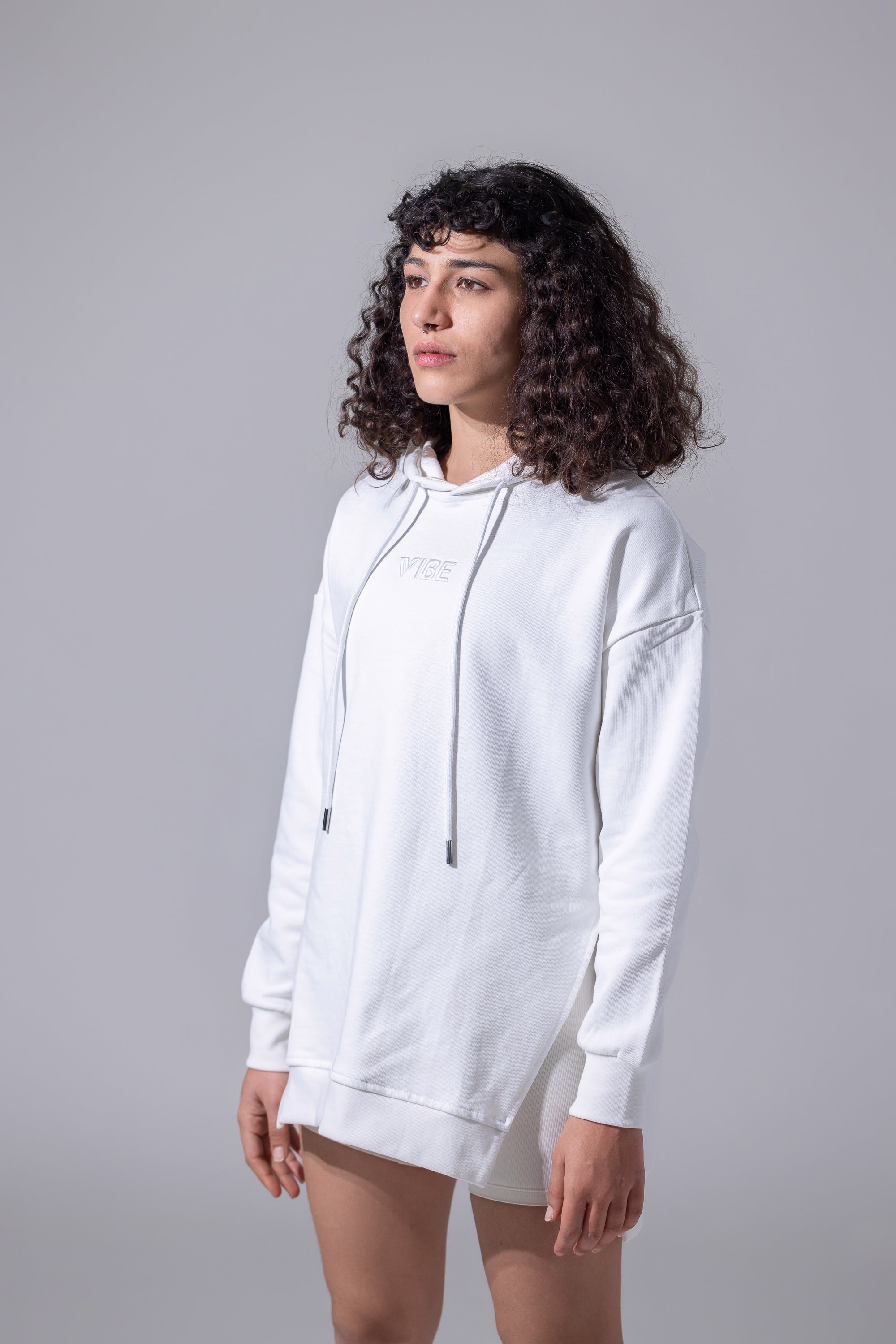 A person standing wearing a white hoodie with a hood, paired with shorts.