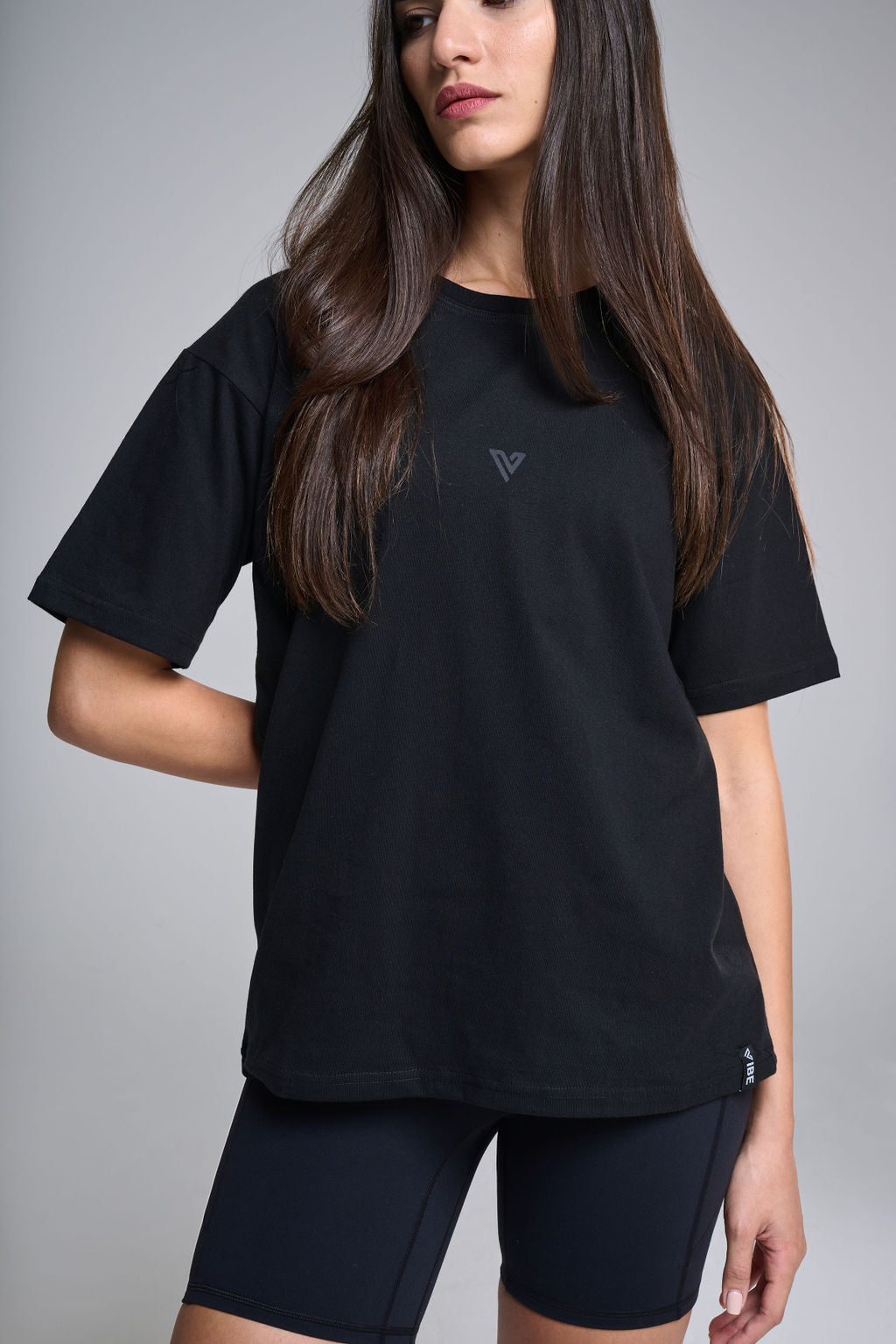 A female model wearing a black oversized T-shirt with short sleeves and a round neckline, paired with black shorts.