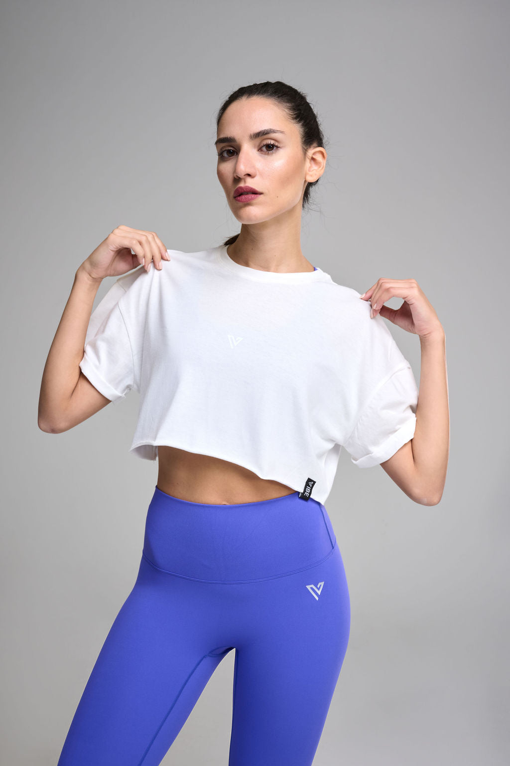 A female model wearing a white crop top and blue activewear pants.