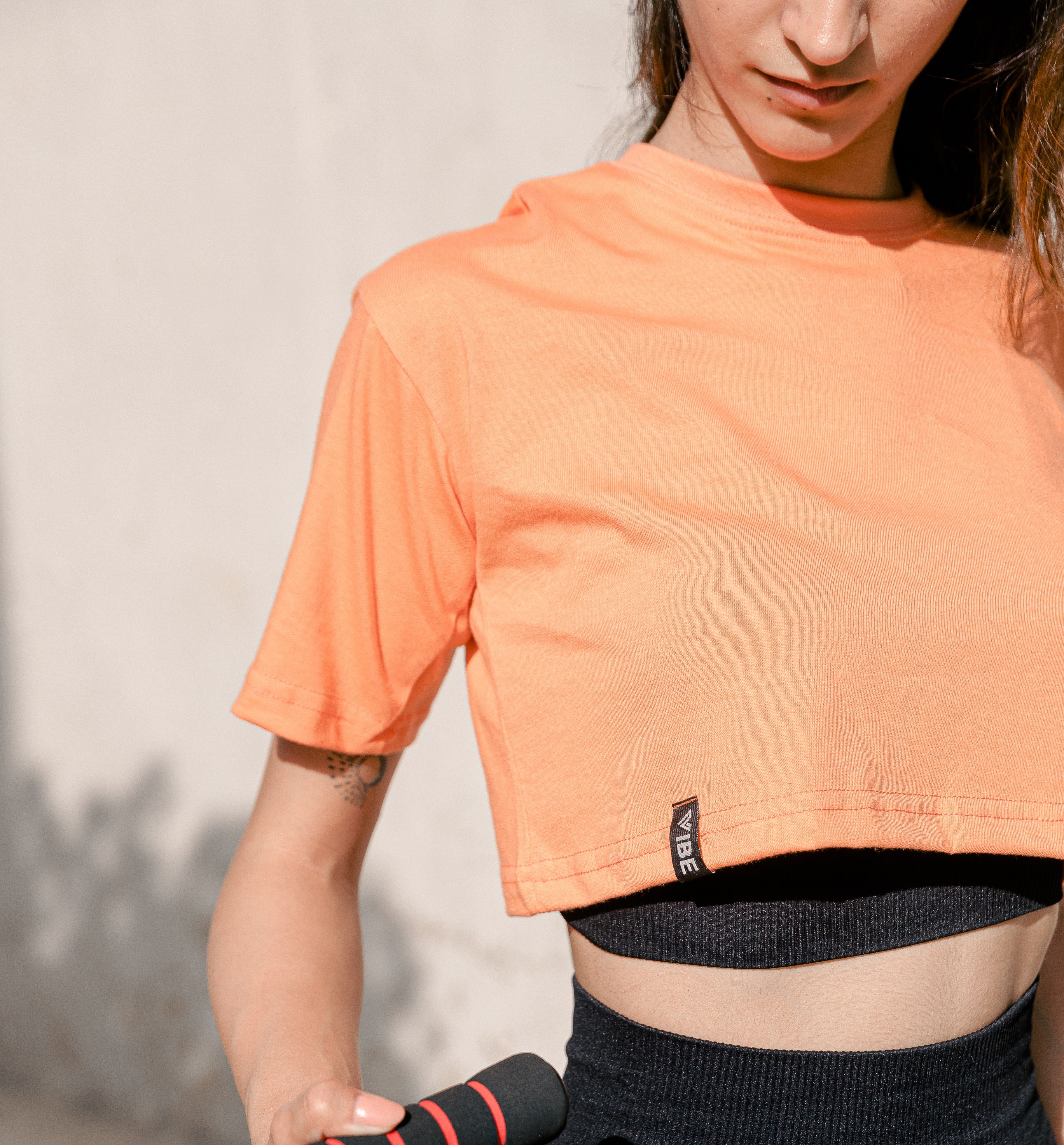 A person wearing an orange crop top and black activewear bottoms, standing in front of a neutral background.