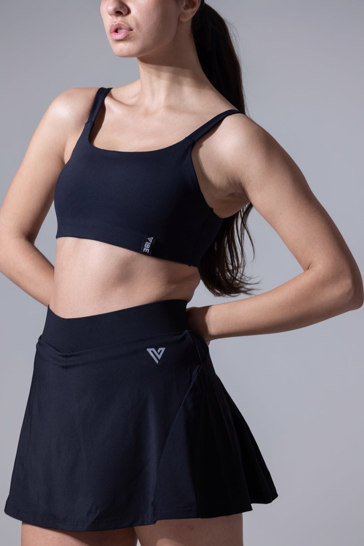 A woman wearing a black sports bra and a matching skirt, standing with one hand on her hip.