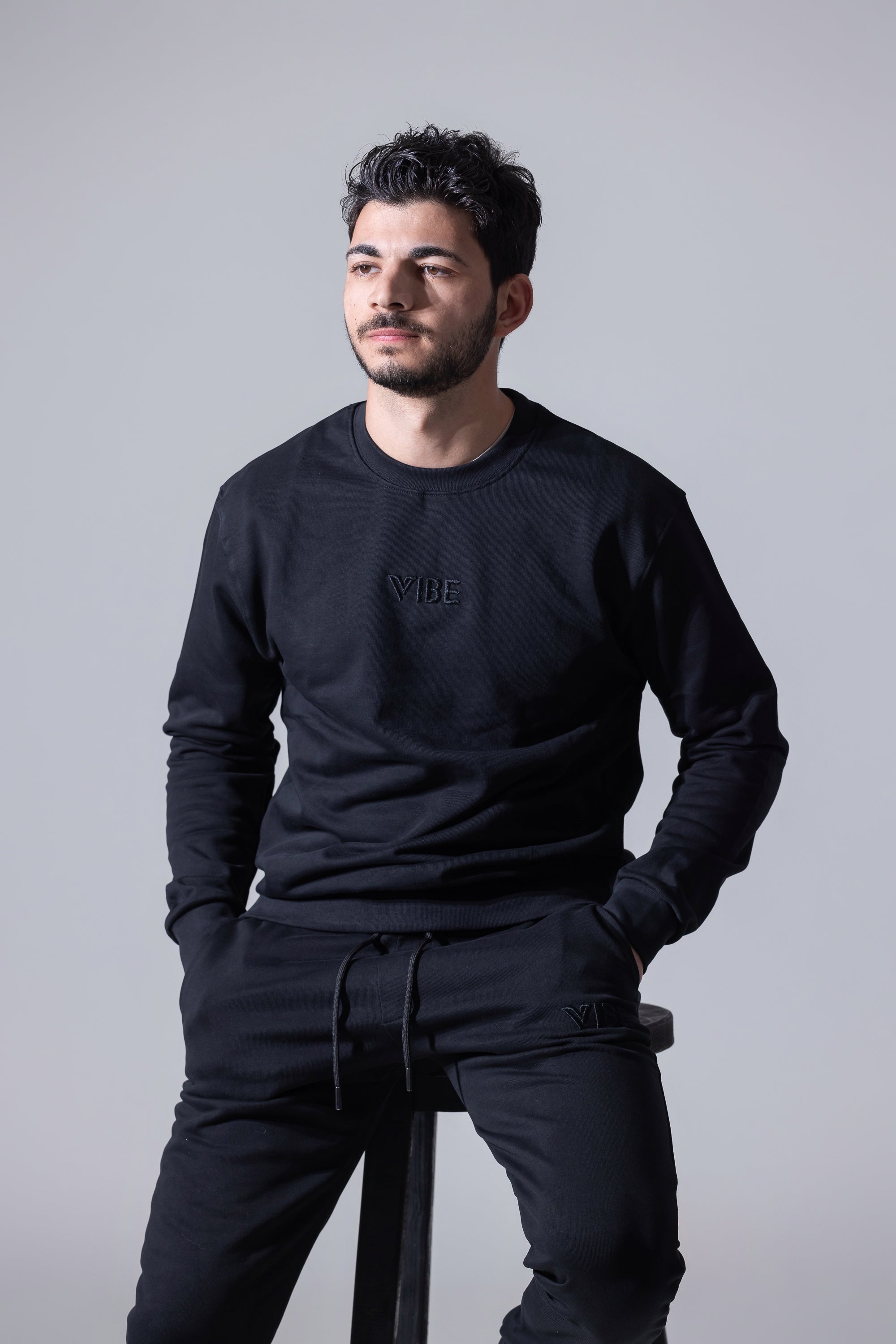 A person sitting on a chair wearing a black long-sleeve crew neck sweater and black pants.