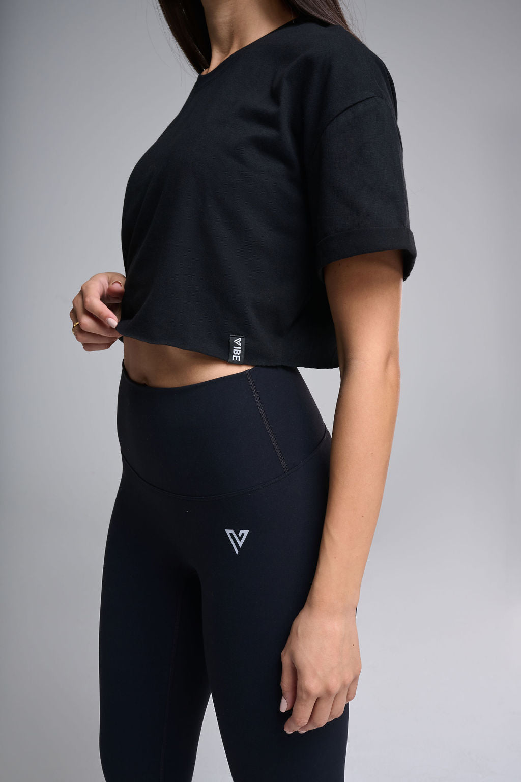 A woman wearing a black crop top and black leggings, with the logo 'V' visible on the crop top.