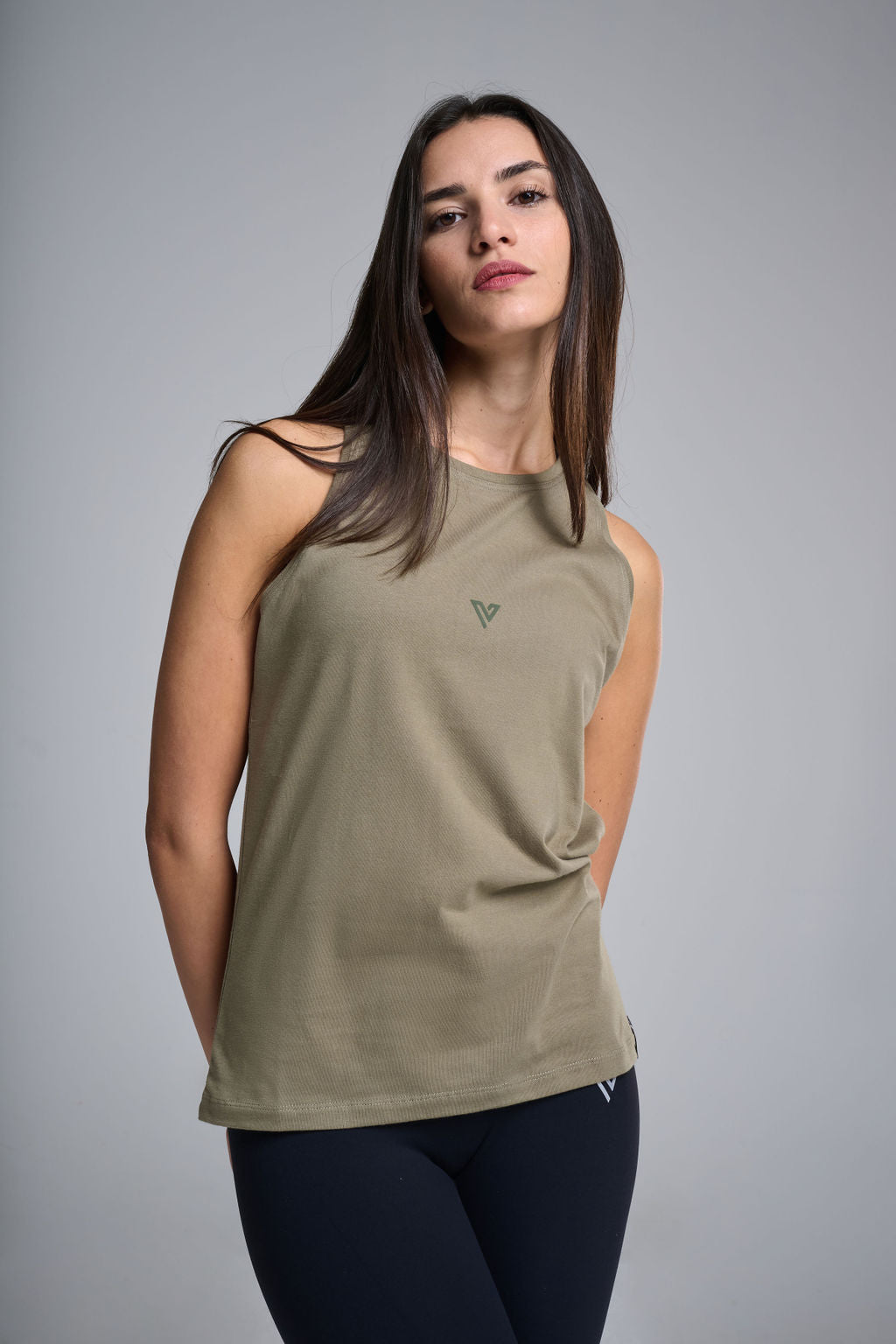 A female model wearing an olive green sleeveless tank top with a round neckline, displaying a small emblem on the chest area.