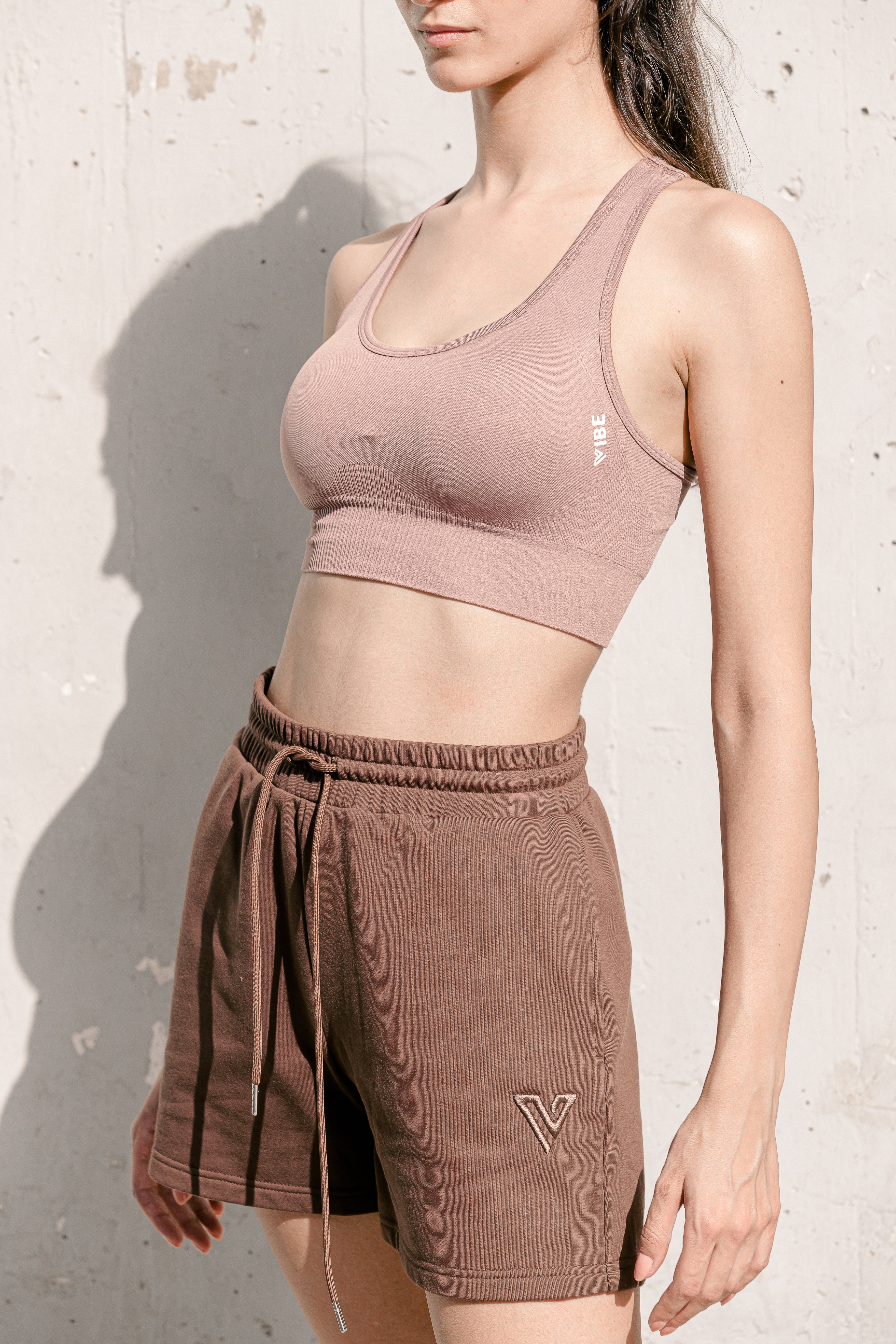 A female model wearing brown sweatshorts with a drawstring waist and a matching brown sports top.